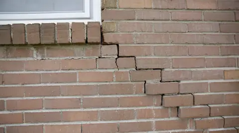 Stair-step crack running down through the mortar joints of a brick wall below a window