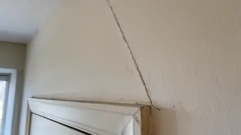 Diagonal crack in drywall running up from the corner of a door frame