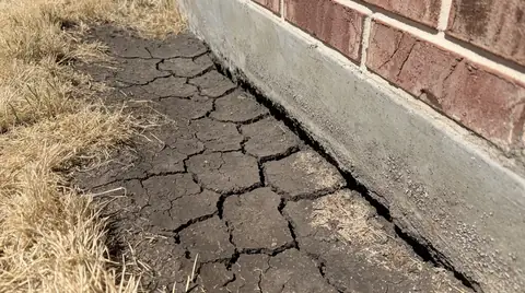 Dry clay soil cracked and pulled away from the edge of a slab foundation